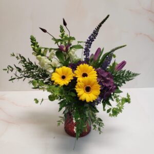 A small floral arrangement of yellows and purples with organic green foliage.