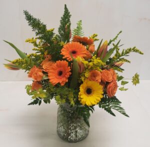 A bright floral arrangement of oranges, yellows, and greens. Features germinis, spray roses, and solidago.