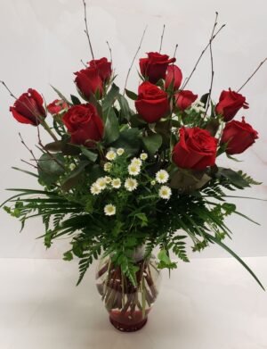 A classic red rose arrangement with small white flowers, in a clear glass container with red rocks.