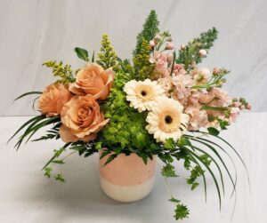 A mix of peach and blush blooms arranged artfully in a peach and cream ceramic container
