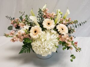 A beautiful and lush combination of blush blooms arranged in a white glass cylinder.