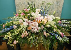beautiful pastel blooms and lush foliage arranged on a casket spray for funerals.