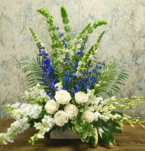 A large arrangement of blue, white and green flowers in a low rectangle container.