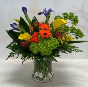 Brightly colored flowers arranged in a clear vase with lush greenery.