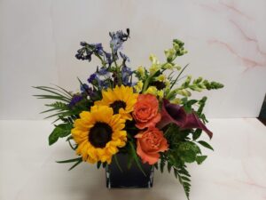 A vibrant mix of flowers like sunflowers and snapdragons in a small square cube