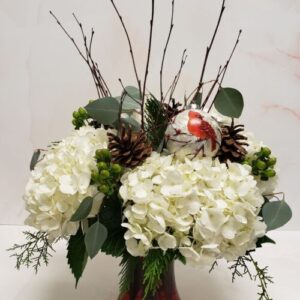 A rustic arrangement of white hydrangeas, pinecones and birch branches with a keepsake ornament