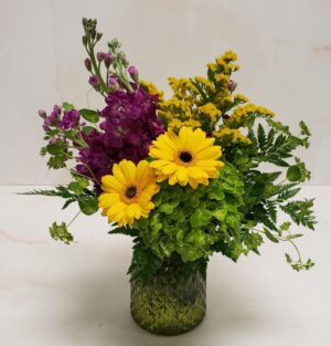 A small arrangement of purple, yellow, and greens in a textured glass container.