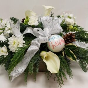 Holiday arrangement of white flowers and mixed holiday greens with a bow and keepsake ornament.