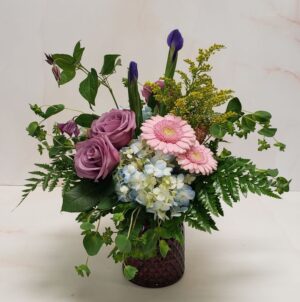 Small arrangement in a textured glass container with pastel blooms and mixed greens.
