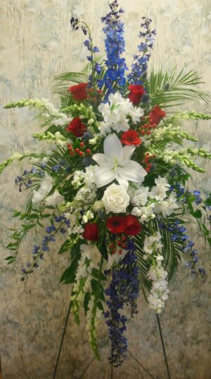 A standing spray arrangement for funerals with red, white, and blue blooms