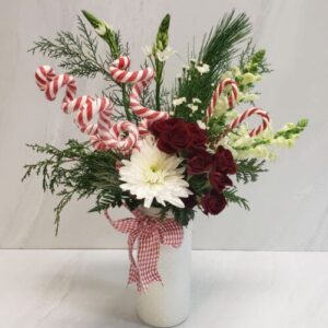 A festive red and white arrangement with holiday greens, holiday decorations, and a bow.