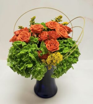 Small boutique arrangement of hydrangeas, roses, and solidago with wooden accents
