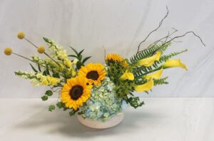 Modern bright floral arrangement of yellows, greens, and blue in a blue and cream ceramic container