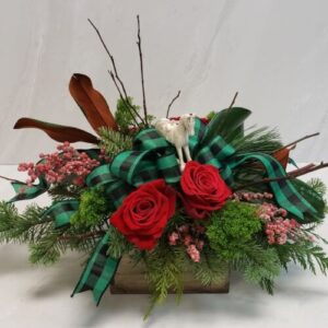 A festive arrangement in a wooden planter box with evergreens and red roses, finished with a bow and a keepsake rocking horse ornament