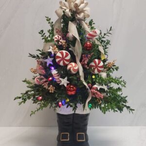 Boxwood branches shaped into a mini, decorated Christmas tree in a ceramic container of santa boots