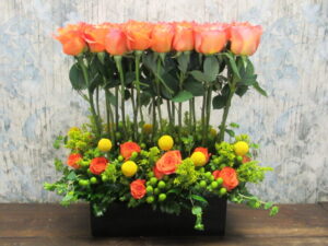 A modern dozen rose arrangement with a lush accent of spray roses, billy balls, and hypericum berries around the base