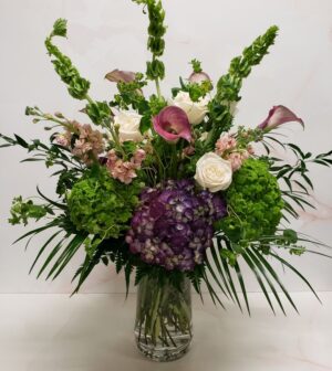 An English garden style arrangement with pink, purple, and cream blooms arranged in a glass vase