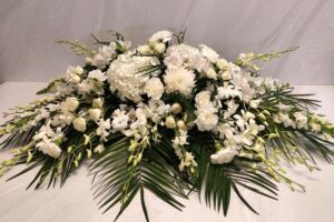 An all white floral casket spray accompanied by robellini palm fronds