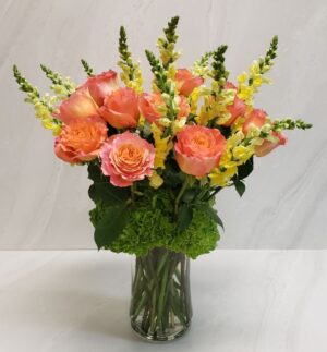 An elegant arrangement of yellow snapdragons, freespirit roses, and green hydrangeas in a glass vase