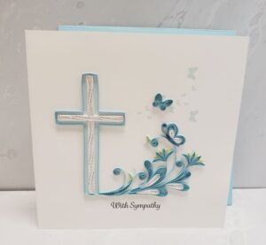 A 6"x6" quilling card that says, "With Sympathy." Features blue and white quilling art of a cross and butterflies.