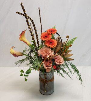 A contemporary arrangement with florals and dried elements arranged in a rustic tin cylinder