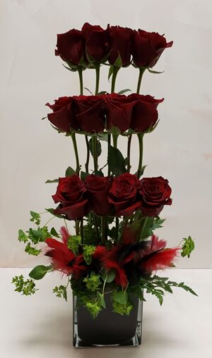 A modern dozen red rose arrangement of varying stacked heights in a black square container