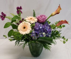 An organic arrangement in a green vase with lots of textures and bright flowers.