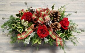 Low centerpiece with red roses, pinecones and holiday greenery finished with a festive bow