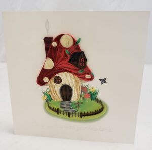 A 6"x6" quilling card of a red toadstool house and yard.