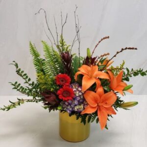 A mix of flowers in warm tones arranged in a garden style in a yellow glass cylinder.
