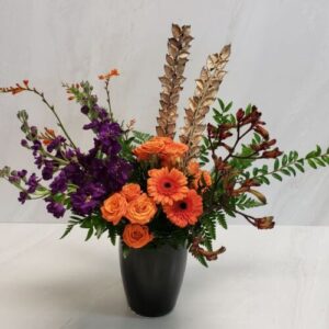 A Halloween themed arrangement with purple and orange blooms in a black glass vase.