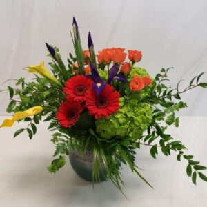A bright combination of flowers in a rounded container with lots of natural greenery