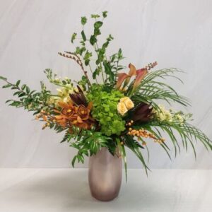 A mixed flower arrangement with lots of rustic foliage, artfully arranged in a champagne colored container.