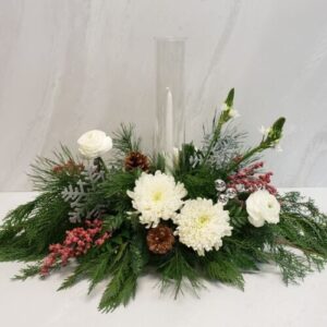 Small holiday table centerpiece with mixed holiday greens and white blooms, accompanied by a tapered candle