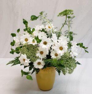 A lush arrangement of daisies, queen anne's lace and bupleurum in a yellow class vase.