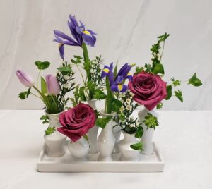 Pink and purple flowers accompanied by textured greenery in a chic ceramic collection of vases