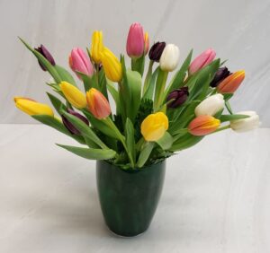 A colorful mix of tulips in a dark green glass container